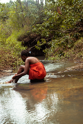 A young black woman sitting by the river washing her feet