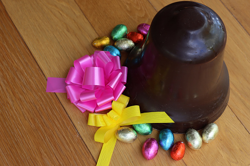 Easter background with chocolate bell with chocolate eggs and pink and yellow bows on a wooden table