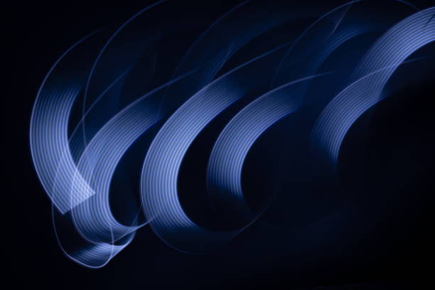 istock Blue neon curved wave of light as curls or swirl with smooth stripes on black background, pattern. Abstract background with motion light effect, light painting in holiday style. 1944435574