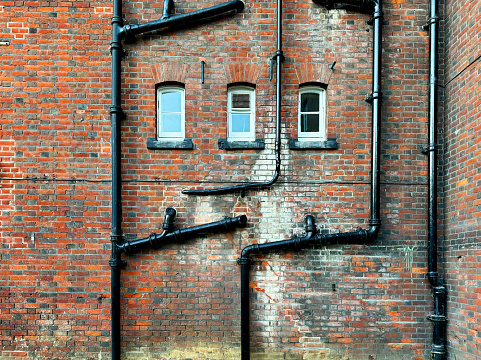Black drain pipes and windows on an old weathered brick wall