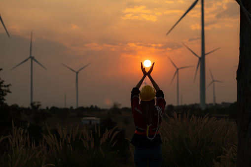 Engineer woman with yellow helmet and wind turbine on sunset background.