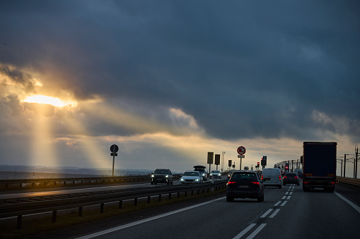 Cars and truck driving on highway at dusk. Dramatic light beams coming through the clouds