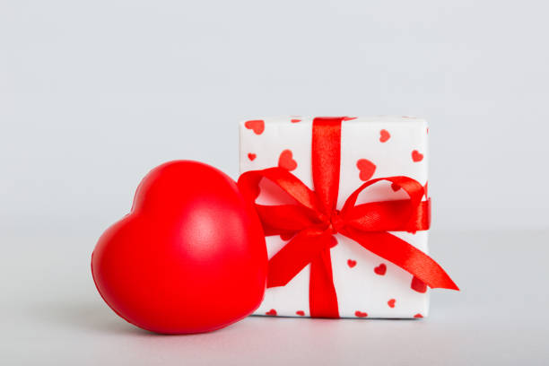 gift box with red bow and red heart on colored background. Perspective view. Flat lay.