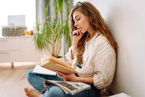 istock Young woman reading a book, writing notes, doing homework at home. 1944525177