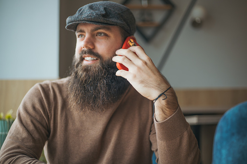 a young modern man with a beard is sitting in a cafe and talking on the phone
