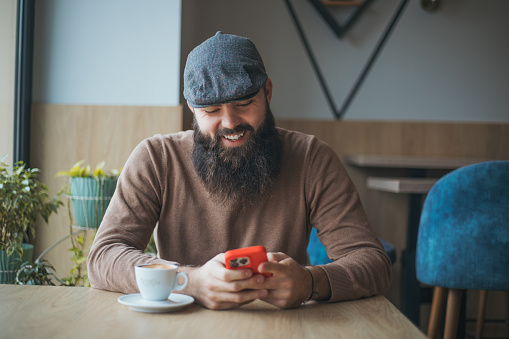 Handsome hipster guy using smart phone in cafe