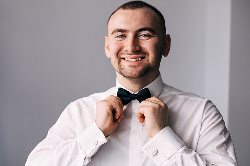 cheerful man the groom smiles, stands in a shirt and a bow tie