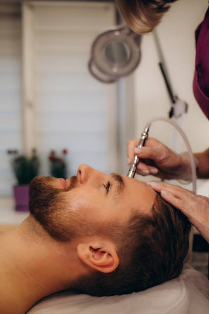 the cosmetologist makes the procedure microdermabrasion of the facial skin of a man in beauty salon. - microdermabrasion stock-fotos und bilder