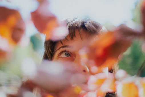 Young woman portrait looking up while hiding behind tree leaves