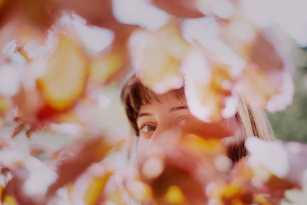Young woman portrait looking at camera while hiding behind tree leaves