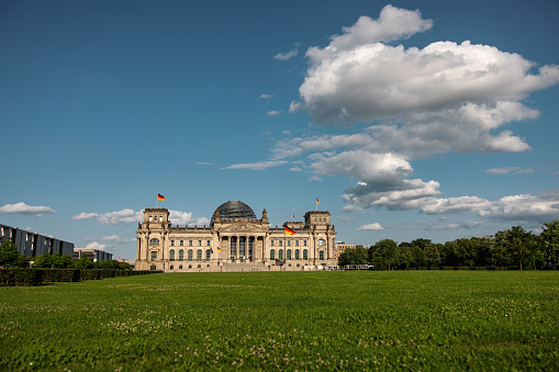 Wide shot of the Reichstag building under blue sky with lush green lawn in the foreground, symbolizing German history and governance.