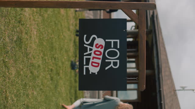 Female real estate agent puts sold sticker on for sale sign