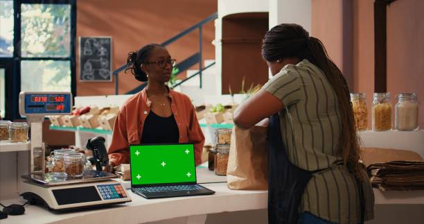 Vendor using a laptop with greenscreen layout at store checkout