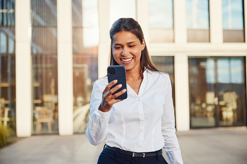 Confident businesswoman walking using her smartphone outside the office