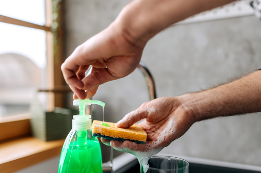 Close up shot of an unrecognisable man putting dish soap on a cleaning sponge