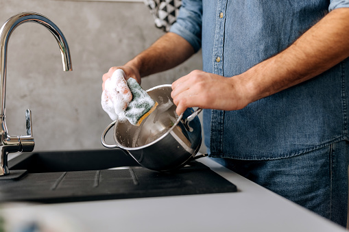 Close up shot of an unrecognisable man washing pot in a domestic kitchen
