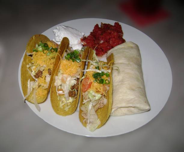 istock Tacos and a burrito with meat, cheese and vegetables on a white plate 1944714383