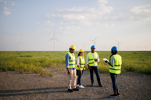 Engineers wearing uniform ,helmet hold document inspection work in wind turbine farms rotation to generate electricity energy.