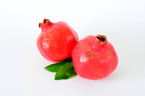 two red pomegranates with green leaves on white background
