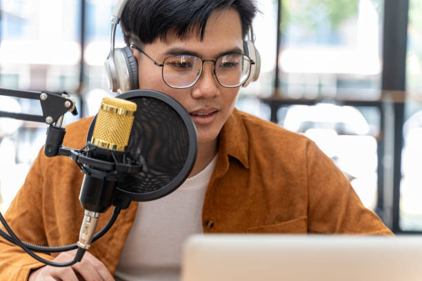 istock Young Asian man speaking to microphone during his live podcast while checking the feedback from his online audiences from his laptop computer 1944729174
