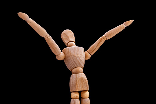 wooden mannequin with hands up on dark background