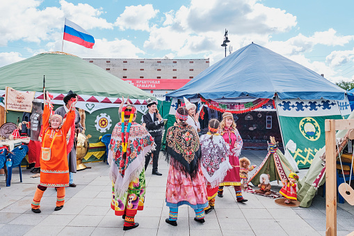 Irbit, Russia - August 11, 2023: Irbit Fair. People in traditional festive clothes of ethnic groups of Urals dancing in front of national courtyards - tents.