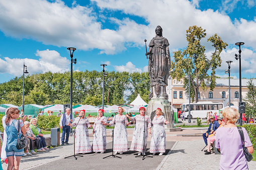 Irbit, Russia - August 11, 2023: Irbit Fair. Five mature women in concert dresses,vocal group, singing in front of audience on Lenin Square. Restored monument to Catherine II by sculptor Mikeshin.