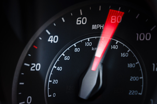 Motion blur as a car's speedometer shows the speed passing 80mph.