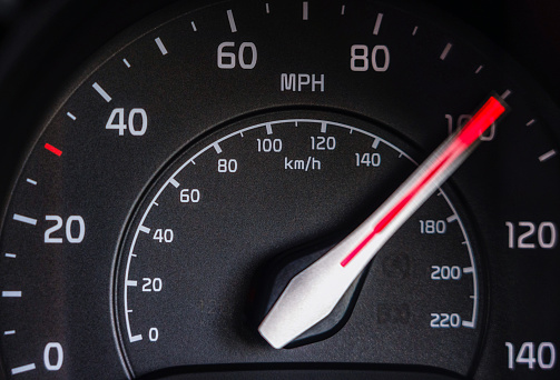 Motion blur on the needle of a car's speedometer as it hits 100mph during a race.