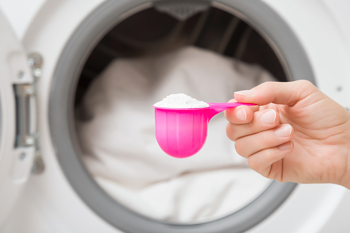 Young adult woman hand holding pink cup or scoop of white powder for clothes washing. Closeup. Front view.