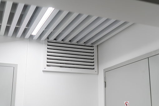 This image shows a large industrial air ventilation unit mounted on a white wall, with venting slats directing airflow within a contemporary building.