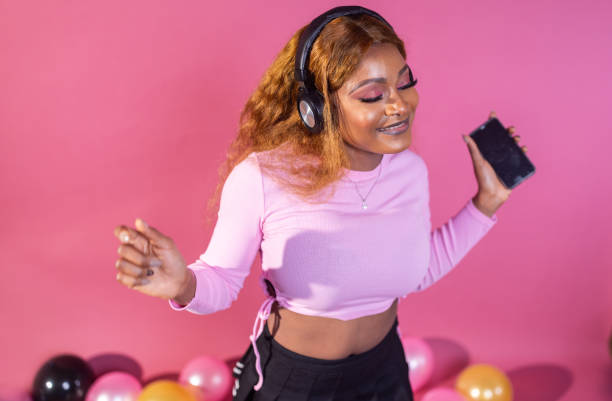 Lost in the music, a woman with headphones moves to the beat, her joyful dance matching the lively backdrop of pink hues and floating balloons.