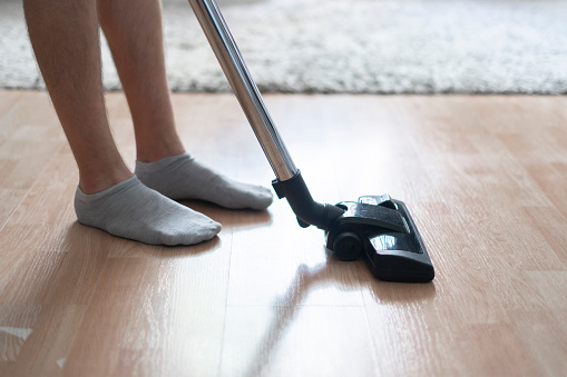 This image captures a close-up view of an individual cleaning a hardwood floor with a contemporary house vacuum cleaner, focusing on the efficiency of domestic chores.