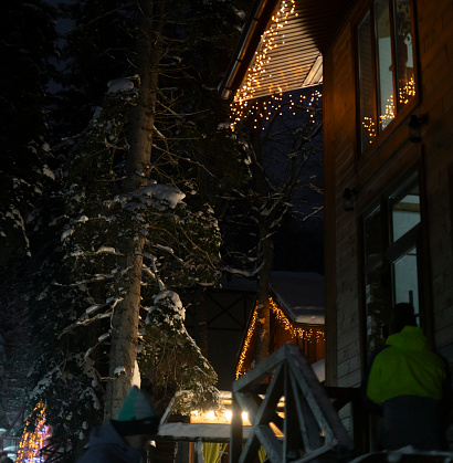 A charming A-frame cabin adorned with string lights stands out against the dark, snowy backdrop of a serene winter night.