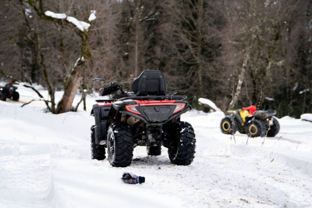 a red and black quad bike stands idle on a snow-covered trail, its presence contrasting with the serene, white winter landscape. - off road vehicle quadbike 4x4 stationary fotografías e imágenes de stock