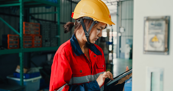 Professional Asian female industrial engineers operating machine keypad in manufacturing factory. Engineering and sustainable production plant concept.