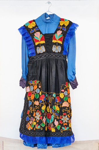 Traditional festive Tatar women's clothing. Old blue dress and black embroidered apron with bright colorful floral intricate patterns in the national style, with frills.