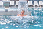 Hydromassage in outdoor thermal swimming pool.Senior caucasian woman enjoying falling jets of water