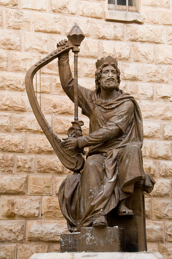 Bronze statue of King David beside a stone wall playing the harp outside his tomb in the Old City of Jerusalem, Israel.