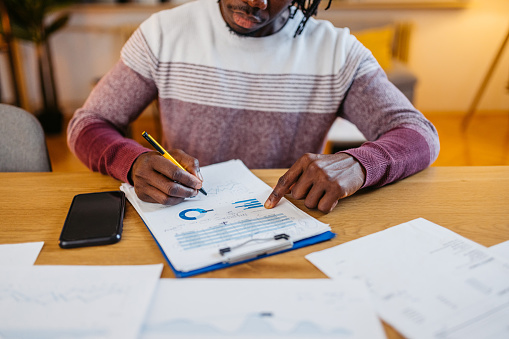 Young black man sitting at the kitchen table and checking his finances at home at night. Close-up.