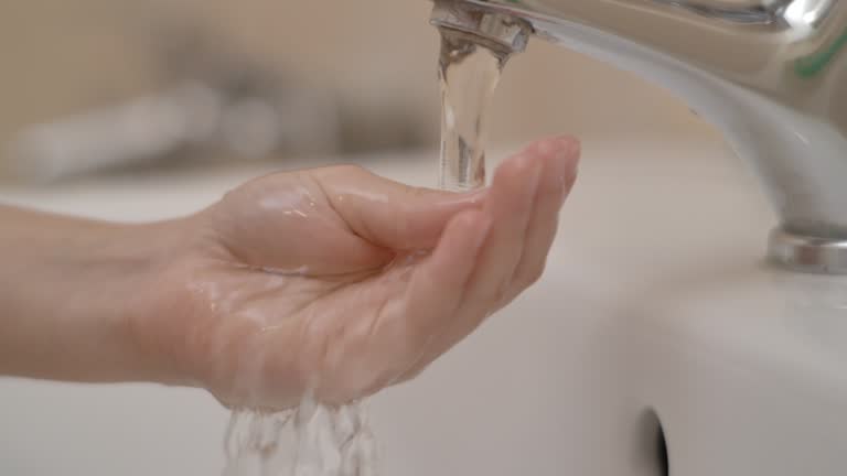 Slow Motion. Closeup of Human Hand Under Stream of Pure Water From Tap. Child Palm Under Stream of Water Slow Motion. Little Girl in Bathroom at Home Checking Temperature Touching Running Water.