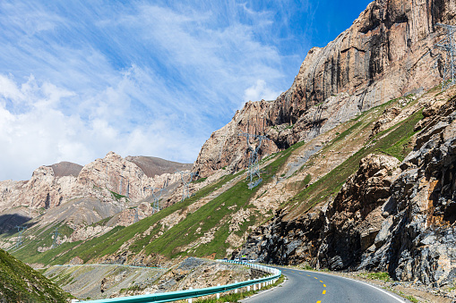 Wide-angle view of the renowned road ascending Passo dello Stelvio (formally known as Strada Statale 38 dello Stelvio), a mountain pass which connects Valtellina and Val Venosta at an elevation of 2,757 metres above sea level, in the Italian Alps, offering breathtaking views on the surrounding mountaintops and the underlying valley. The dazzling bright light of a summer noon, a perfectly clear sky, rough rocky cliffs and steep green slopes, cyclists, bikers and cars following the narrow, winding strip of asphalt. High level of detail, natural rendition, realistic feel. Developed from RAW.