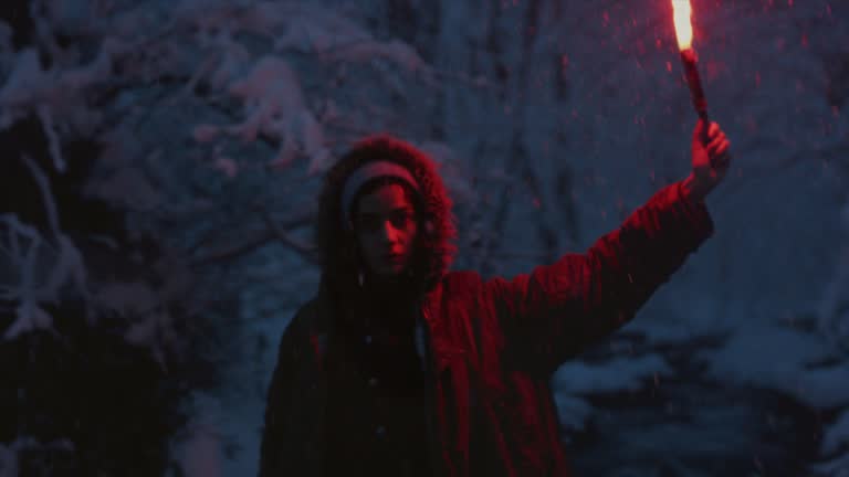 A young girl holding a burning signal fire. A woman in a winter forest lights a red rescue flare