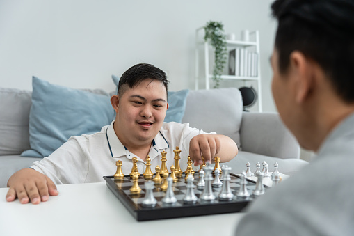 Asian attractive father play chess game with his son in living room. Happy family, Young family feeling happy and relax, spending free leisure time together in house. Relationship lifestyle concept.
