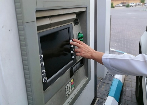 Arab man's hand with white long sleeve using drive through ATM from inside the car to withdraw money.