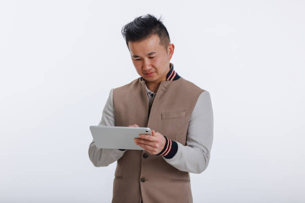 East Asian businessman in a casual suit intently using a digital tablet against a white background.