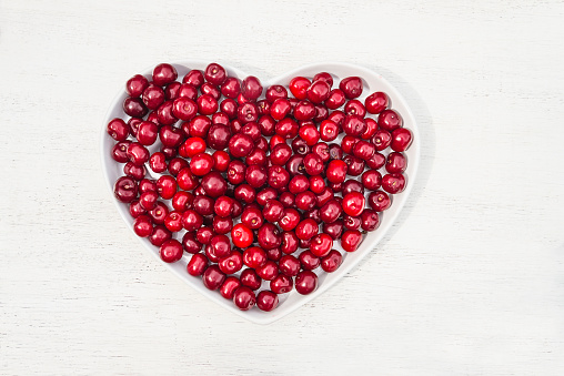 Red ripe cherries in a white bowl shape heart on a white background