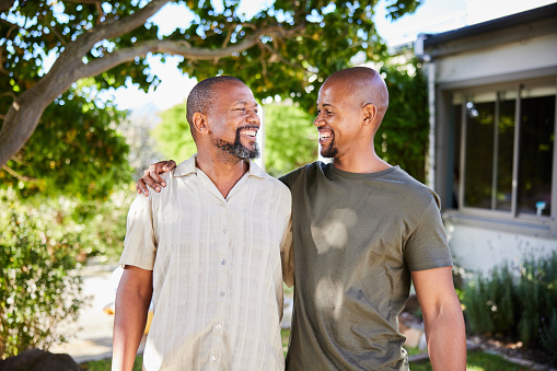 mature man and his adult son laughing while standing arm in arm together outside in a back yard at home