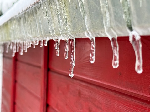 Visible is the edge of the roof of an typical Swedish house. The wall is made of wood. Icicles are dripping down.