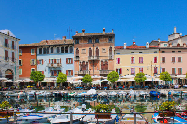 A row of terraces and restaurants along the marina in Desenzano del Garda with colorful houses and boats.